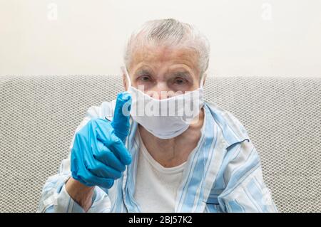 Une femme âgée montre le pouce pour lutter avec COVID-19 en portant un masque d'hygiène et des gants de protection. Concept de protection contre le coronavirus Banque D'Images