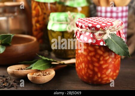 Pots avec légumes marinés, haricots, épices et ustensiles de cuisine sur fond en bois Banque D'Images