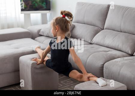 Petite fille mignonne pratique la gymnastique à la maison. Formation en ligne. Étirements, ficelle. Quarantaine. Restez à la maison Banque D'Images