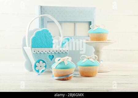 Délicieux cupcakes avec noeud et chaussures de bébé, chariot de bébé décoratif et album photo sur fond de couleur Banque D'Images