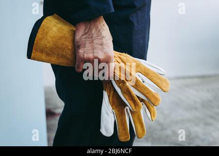 La main du technicien mécanicien tient des gants en cuir en se tenant devant de l'atelier d'entretien, préparation du technicien de maintenance technique f Banque D'Images