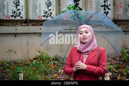 Une pose touristique pour une photo devant les fûts de saké à l'entrée du sanctuaire Meiji, un dimanche matin pluvieux, à Tokyo, Japon Banque D'Images