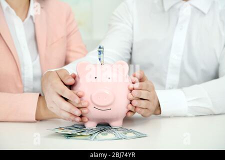 Un jeune couple heureux tenant dans la banque de piggy mains avec des billets en dollars. Concept d'économies d'argent Banque D'Images