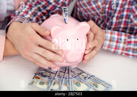 Un jeune couple heureux tenant dans la banque de piggy mains avec des billets en dollars. Concept d'économies d'argent Banque D'Images