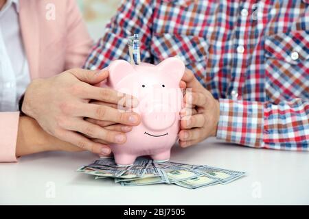 Un jeune couple heureux tenant dans la banque de piggy mains avec des billets en dollars. Concept d'économies d'argent Banque D'Images