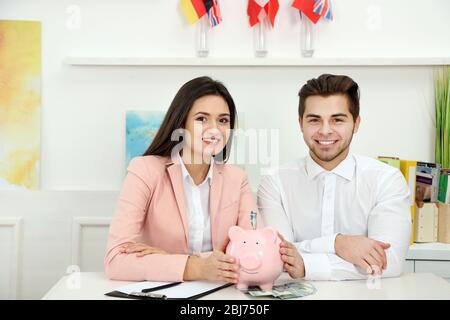 Un jeune couple heureux tenant dans la banque de piggy mains avec des billets en dollars. Concept d'économies d'argent Banque D'Images