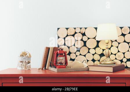 Intérieur de la chambre avec commode en bois rouge, lampe et lanterne sur fond de mur clair Banque D'Images