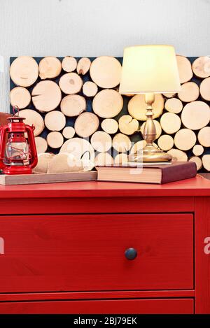 Intérieur de la chambre avec commode en bois rouge, lampe et lanterne sur fond de mur clair Banque D'Images