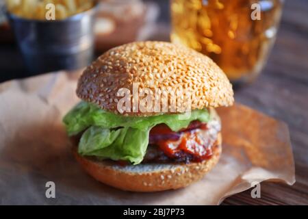 Gros hamburger savoureux sur un papier avec bière légère dans un mug en verre, gros plan Banque D'Images