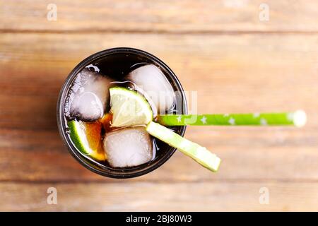 Cocktail avec tranches de citron vert et blocs de glace sur table en bois, gros plan Banque D'Images