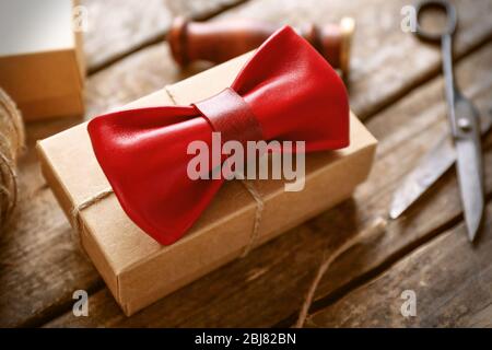 Noeud papillon en cuir rouge et boîte cadeau en carton avec joint rouge sur table en bois, gros plan Banque D'Images