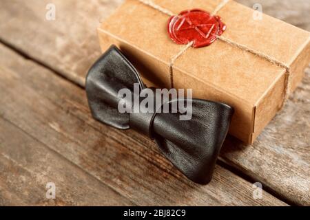 Noeud papillon en cuir noir et boîte cadeau en carton avec joint rouge sur table en bois, gros plan Banque D'Images