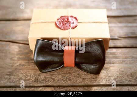 Noeud papillon en cuir noir et marron et boîte cadeau en carton avec joint rouge sur table en bois, gros plan Banque D'Images