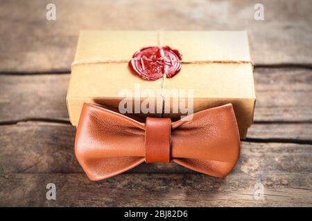 Noeud papillon en cuir marron et boîte cadeau en carton avec joint rouge sur table en bois, gros plan Banque D'Images