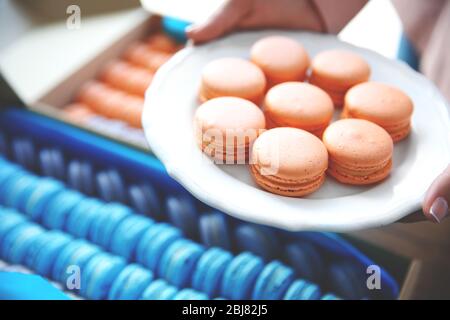 Mains féminines tenant de savoureux macarons sur la plaque blanche, gros plan Banque D'Images