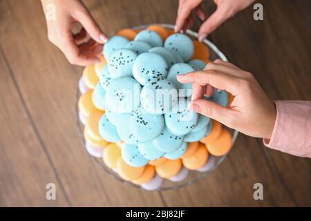 Mains féminines prenant de savoureux macarons de plat sur la table Banque D'Images