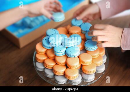 Mains féminines prenant de savoureux macarons de plat sur la table Banque D'Images