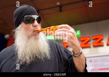 Homme mûr barbu mangeant de la pizza pepperoni de style New York à l'extérieur Banque D'Images