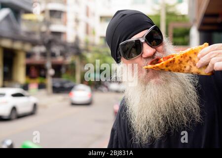 Homme mûr barbu mangeant de la pizza pepperoni de style New York à l'extérieur Banque D'Images