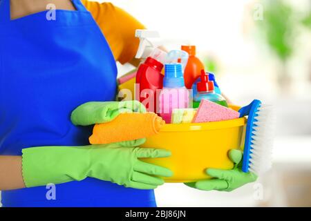 Femme dans des gants en caoutchouc tenant un bassin avec des détergents sur fond flou Banque D'Images