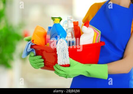 Femme dans des gants en caoutchouc tenant un bassin avec des détergents sur fond flou Banque D'Images