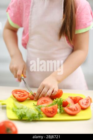 Petite fille coupe des légumes pour la salade dans la cuisine Banque D'Images