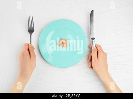 Les mains féminines tenant la lame et la fourchette à côté d'une plaque avec des carottes sur une table en bois blanc Banque D'Images