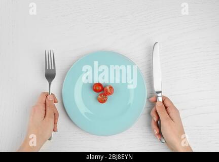 Les mains féminines tenant la lame et la fourchette à côté d'une plaque avec des carottes sur une table en bois blanc Banque D'Images