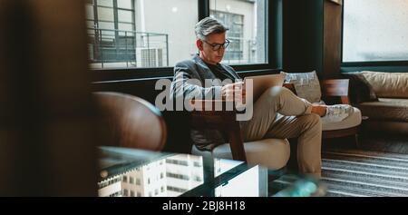 Homme d'affaires mûr assis dans le hall de bureau avec un ordinateur portable. Homme de direction travaillant dans le salon de bureau. Banque D'Images