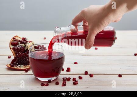 La main verse le jus de grenade d'une bouteille de verre dans un verre. Ouvrez des grenades et des grains sur une table lumineuse rustique. Banque D'Images