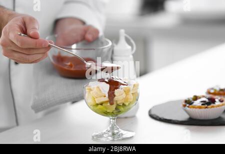 Main masculine verser la sauce au chocolat sur le dessert aux fruits. Banque D'Images