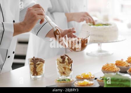 Chef mâle qui verse de la sauce au chocolat sur un dessert aux fruits. Banque D'Images