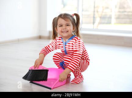 Petite fille avec balai et pelle dans la cuisine Banque D'Images