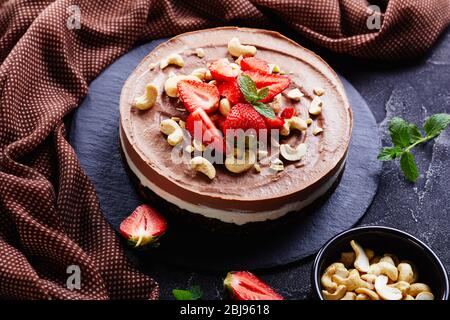 Gâteau simple sans cuisson à la mousse au chocolat fait de crème de noix de coco et de noix de cajou trempées avec la croûte de dattes brutes, de cacao et de pacanes avec fraises et fre Banque D'Images