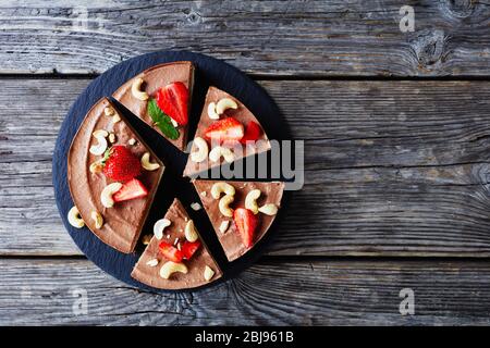 Facile été sans cuisson Triple tarte au chocolat en couches faite de crème de noix de coco et de noix de cajou trempées avec la croûte de dattes brutes, de cacao, et de noix avec paille Banque D'Images