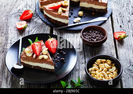 Tarte au chocolat végétarien au dessert de deux couches de crème de noix de coco et de noix de cajou trempées avec croûte de dattes brutes, de cacao et de noix sur une plaque noire Banque D'Images