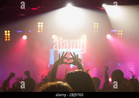 Foule de fans méconnaissables se joignant les mains en forme de cœur tout en exprimant l'amour par rapport à l'interprète au concert Banque D'Images