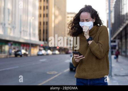 Femme caucasienne portant un masque de protection et toussant dans la rue Banque D'Images