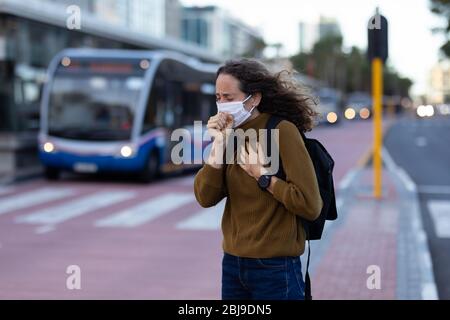 Femme caucasienne portant un masque de protection et toussant dans la rue Banque D'Images