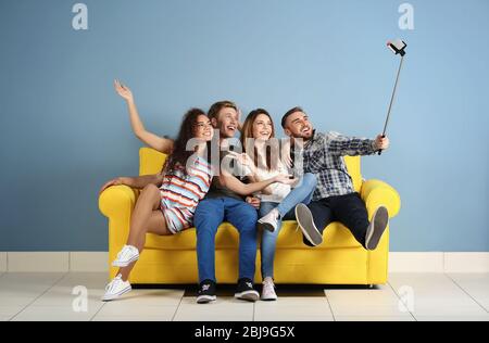 De jeunes amis joyeux prenant selfie sur un canapé jaune dans la chambre Banque D'Images