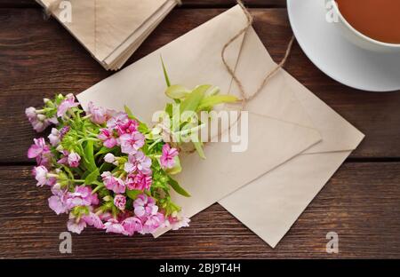 Bouquet de fleurs de prairie avec thé et enveloppes sur table en bois Banque D'Images