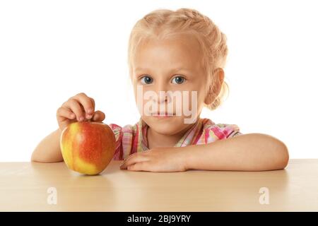Drôle petite fille se cachant derrière la table et regardant la pomme Banque D'Images