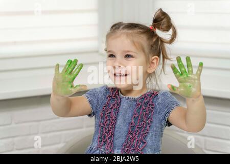 Petite fille peint avec les doigts.fille sourires et montre ses palmiers verts dans la peinture, auto-isolation, coronavirus covid-19, rester à la maison Banque D'Images