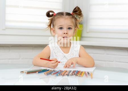 La petite fille de 4 ans dans un masque jetable attire des crayons à la maison à la table. La créativité des enfants sur l'auto-isolation à la maison Banque D'Images