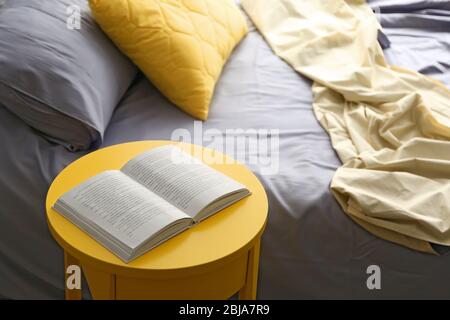 Livre ouvert sur une table de chevet jaune près d'un lit froissé Banque D'Images