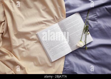 Livre ouvert et belle fleur sur un lit froissé Banque D'Images