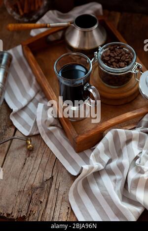 Une tasse de café sur un plateau en bois, du Turk et des grains de café. Faites cuire le petit déjeuner à la maison. Toujours la vie avec un verre avec Cezve. Nappe rayée sur Banque D'Images