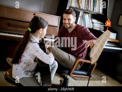 Jolie petite fille jouant de la guitare avec son professeur de musique dans l'appartement rustique Banque D'Images