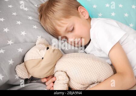 Adorable petit garçon dormant avec un ours en peluche au lit Banque D'Images