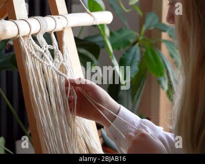 restez à la maison. travail pendant la quarantaine - une fille dans le salon tissage mural des cordes dans la technique macrame. Banque D'Images
